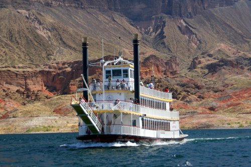 A paddleboat cruises on a lake, surrounded by colorful rocky cliffs and desert landscape.