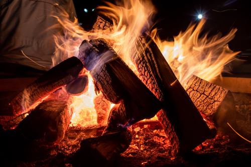 A vibrant campfire with flames dancing around stacked logs, illuminating the dark surroundings.