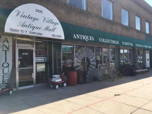 Exterior of Vintage Village Antique Mall, featuring a green awning, various antiques, and collectibles on display.