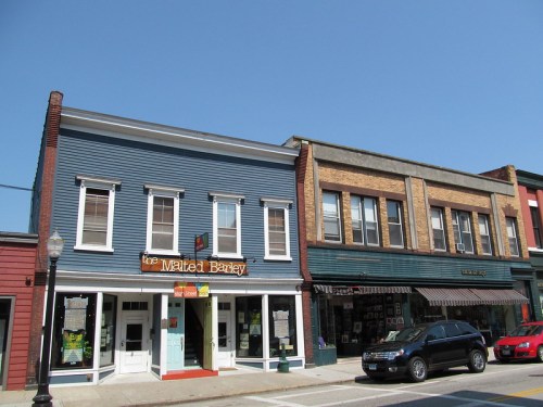 A blue building with a sign for "The Malted Barley" next to a brick storefront, under a clear blue sky.