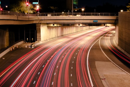 Long exposure shot of a highway at night, showing streaks of car lights and illuminated overpass.