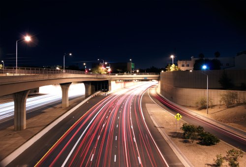 A night view of a highway with light trails from moving vehicles and illuminated streetlights.