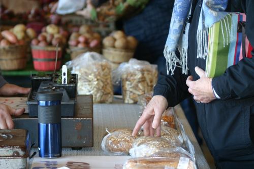A person reaches for baked goods at a market stall, surrounded by baskets of produce and other items.