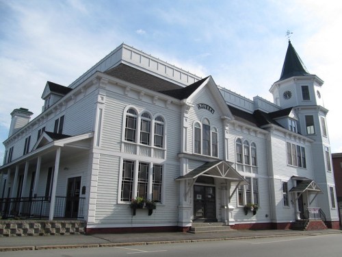 Historic white building with a pointed tower and decorative windows, set against a blue sky.