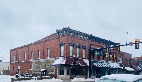 Historic brick building with a snow-covered street, featuring a sign for "More Mint" and a traffic light nearby.