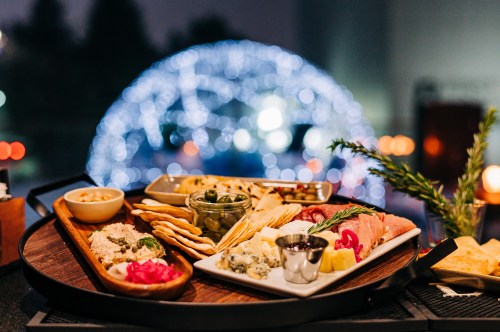 A beautifully arranged charcuterie board with various cheeses, meats, and dips, set against a blurred festive background.