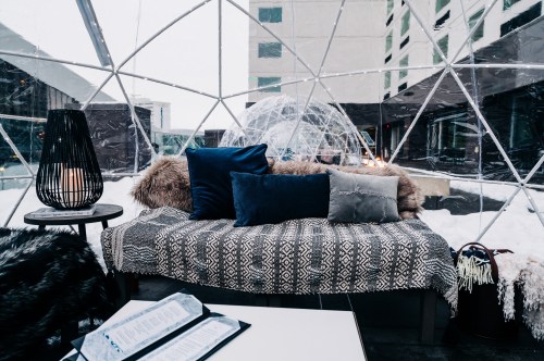 Cozy igloo-style seating area with plush pillows, a warm blanket, and a menu on a table, surrounded by snow.
