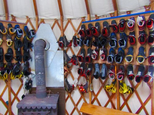 A wall of colorful shoes hanging in a yurt, with a wood stove in the foreground.