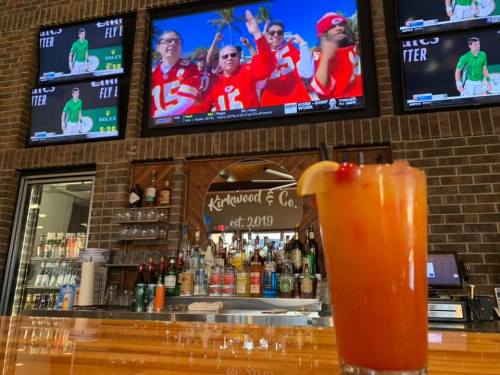 A vibrant bar scene with a colorful cocktail in the foreground and fans cheering on a sports game on multiple screens.