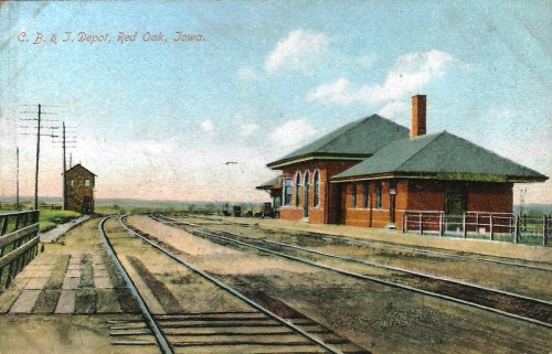 Historic train depot in Red Oak, Iowa, with tracks and a signal tower under a clear blue sky.