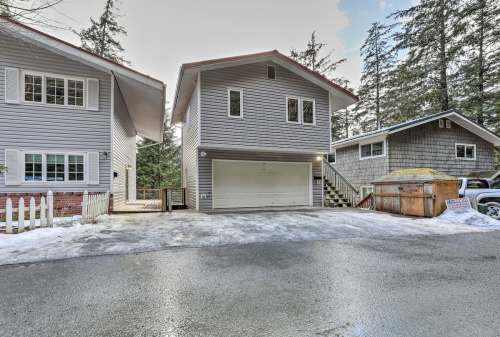 A modern two-story house with a garage, surrounded by trees and snow on the ground, in a quiet neighborhood.