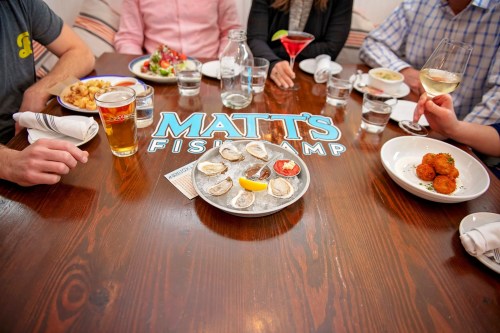 A table at Matt's Fish Camp with oysters, drinks, and various dishes, surrounded by diners enjoying their meal.