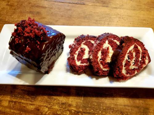 A plate with a chocolate-covered red velvet cake and three slices showcasing cream filling and red velvet layers.