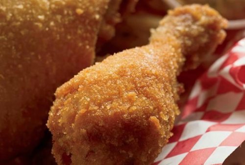 Close-up of a crispy fried chicken drumstick on a red and white checkered paper.
