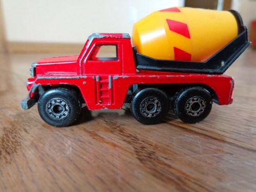 A red toy truck with a yellow cement mixer on the back, sitting on a wooden surface.