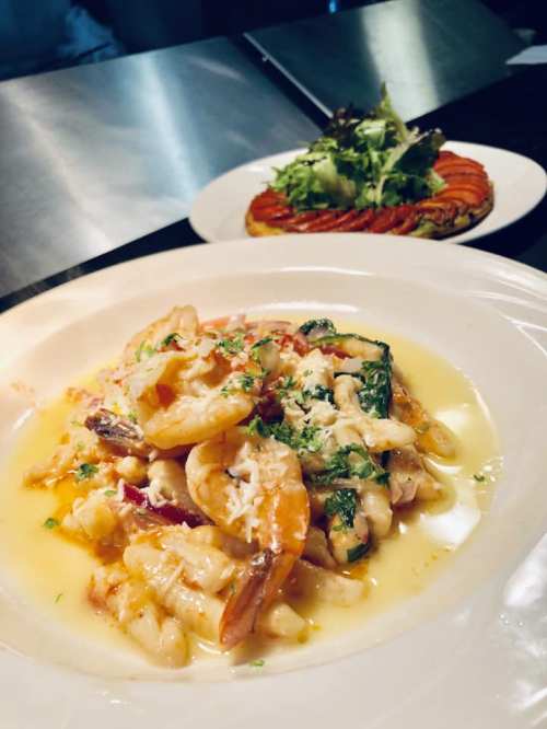 A plate of shrimp pasta in a creamy sauce, with a side salad and a colorful vegetable dish in the background.