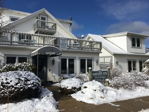 A snow-covered building with a sign reading "Bayside Inn" and an office entrance, surrounded by shrubs.