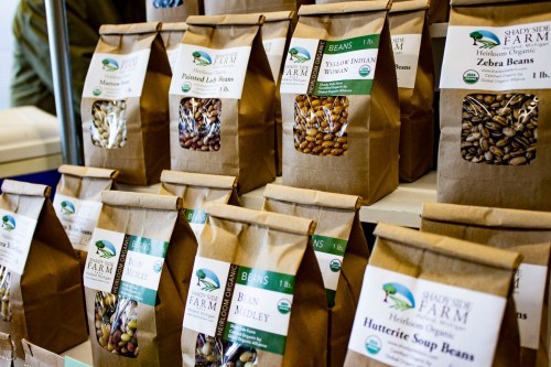 Brown paper bags filled with various types of beans, labeled with names and weights, displayed on a table.
