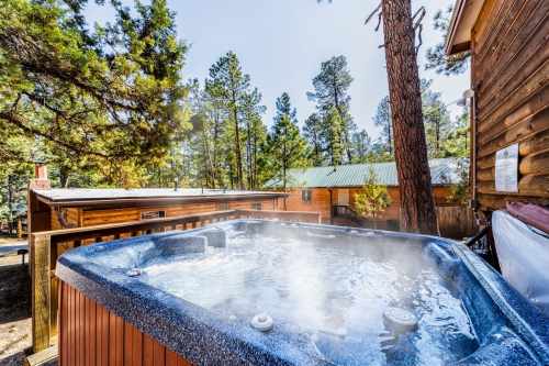 A hot tub with steam rising, surrounded by tall trees and wooden cabins in a serene outdoor setting.