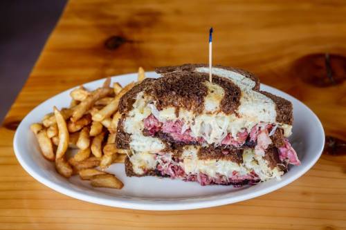 A stacked sandwich with corned beef and sauerkraut on rye bread, served with a side of crispy fries.