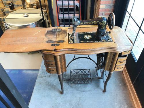 Antique sewing machine on a wooden table with drawers, featuring a decorative design and a metal base.
