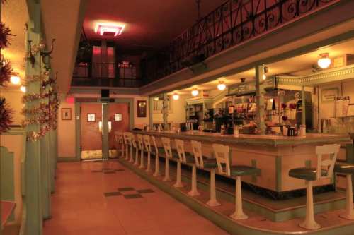 A vintage diner interior with a long counter, bar stools, and retro decor, illuminated by warm lighting.