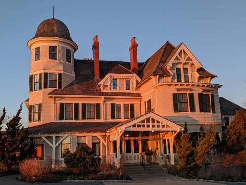A large, historic Victorian house with a turret, featuring intricate architectural details and warm sunset lighting.