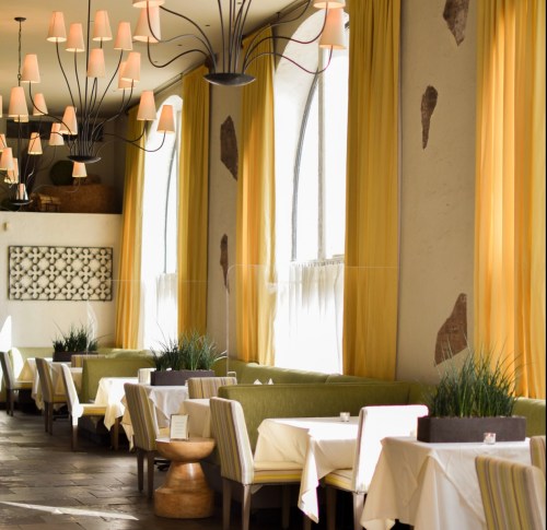 A modern restaurant interior with yellow curtains, green seating, and stylish lighting fixtures.