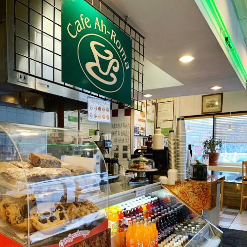 Interior of Cafe Ah-Roma featuring a display case with baked goods and a beverage fridge, with a green sign above.