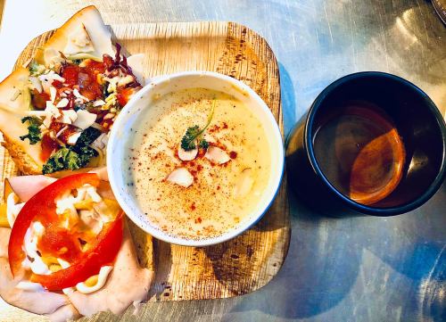 A wooden plate with soup, a sandwich topped with vegetables, and a cup of tea.