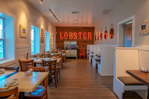 Interior of a cozy restaurant with wooden decor, featuring a "LOBSTER" sign and empty tables ready for diners.