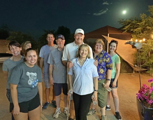 A group of nine people poses together outdoors at night, with a full moon visible in the background.