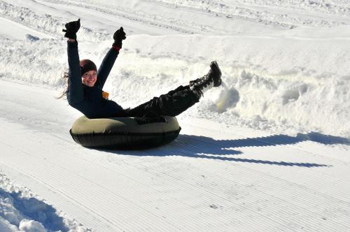 A person joyfully tubing down a snowy slope, arms raised in excitement, with fresh snow all around.