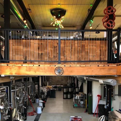 Interior of a brewery with a wooden balcony, metal brewing equipment, and industrial decor.