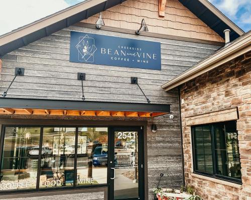 Exterior of Creekside Bean & Wine, featuring a wooden facade and a sign for coffee and wine. Large windows visible.