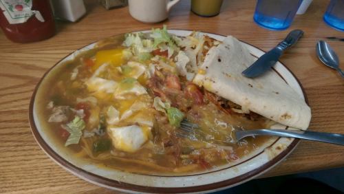 A plate of hearty breakfast featuring eggs, vegetables, hash browns, and a tortilla on a wooden table.