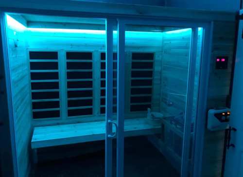A modern sauna with wooden walls, benches, and blue ambient lighting.