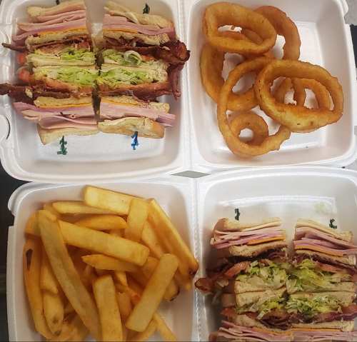 Two containers of sandwiches with layers of meat and lettuce, accompanied by onion rings and French fries.