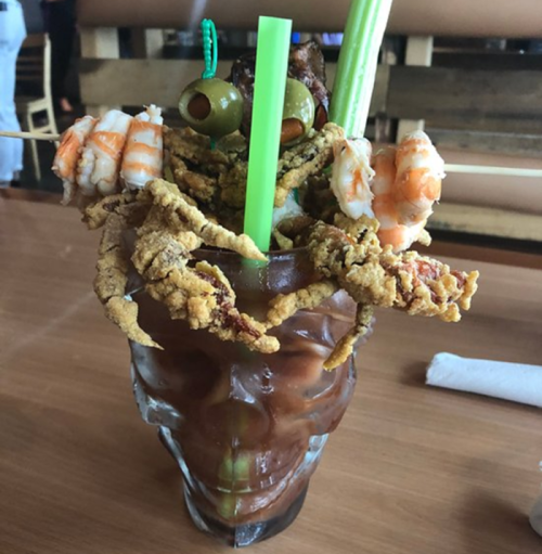 A skull-shaped glass filled with a colorful seafood cocktail, topped with shrimp, olives, and fried seafood.