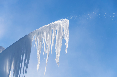 Icicles hang from a snowy peak against a clear blue sky, glistening in the sunlight.
