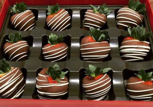 A box of 12 chocolate-covered strawberries drizzled with white chocolate and topped with green leaves.