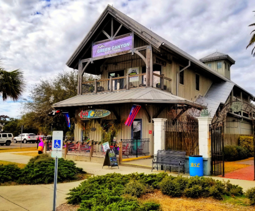 A two-story wooden building with a sign for "Green Canyon," surrounded by greenery and a parking area.