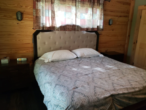 Cozy bedroom with a large bed, two pillows, wooden walls, and a window with patterned curtains.