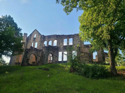 Ruins of a stone building surrounded by trees and grass under a clear blue sky.