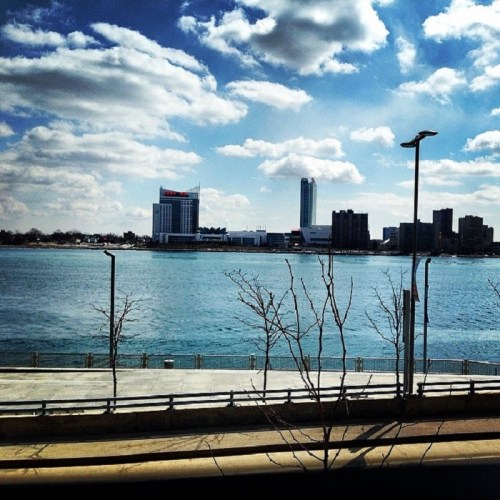 A view of a river with buildings and a cloudy sky in the background, featuring a waterfront promenade.