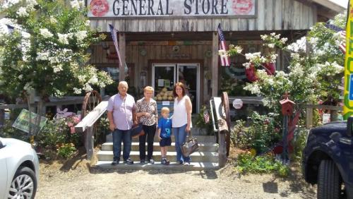 A family stands outside a charming general store, surrounded by flowers and vintage signs.