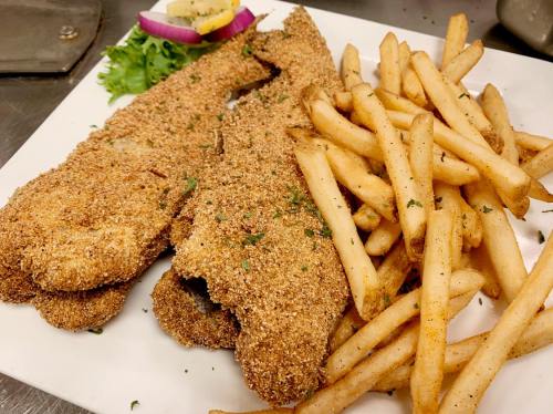 A plate of golden-brown fried fish fillets served with crispy French fries and garnished with vegetables.