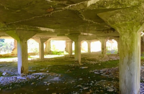 Abandoned structure with concrete pillars, overgrown with moss and surrounded by scattered stones and debris.