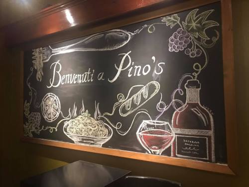 Chalkboard menu with "Benvenuti a Pino's" and illustrations of pasta, wine, grapes, and other Italian food items.