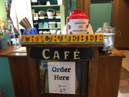 A café counter with a sign reading "Tricklebee Café," a donation jar, and a "Order Here" sign.